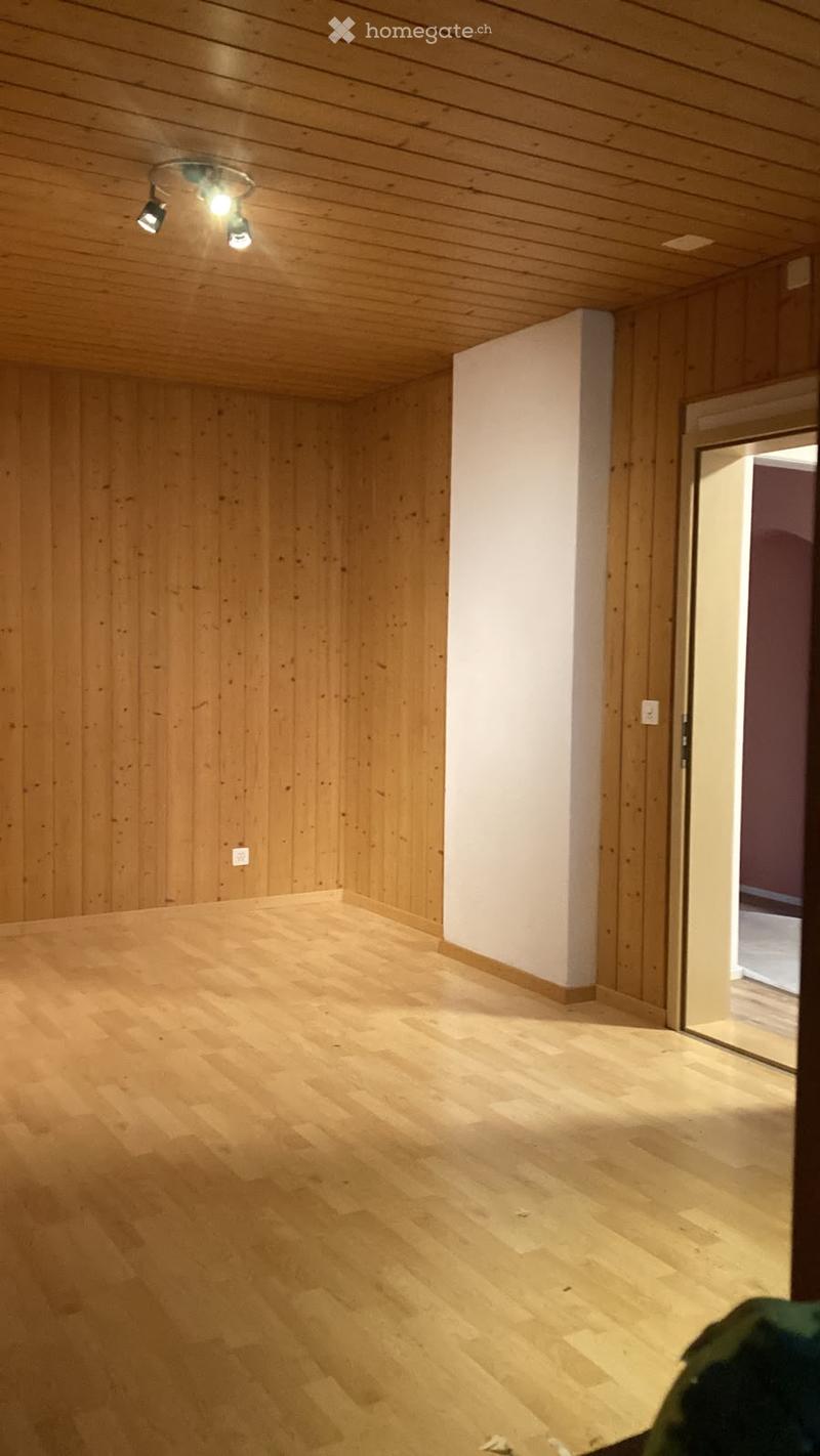 Empty room with wooden walls and floor, exposed wooden ceiling, recessed lighting, and a doorway leading to another space.