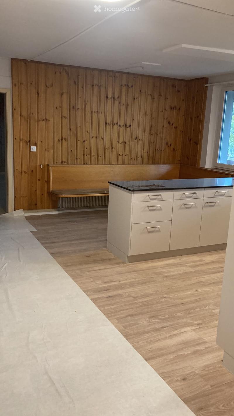 Modern kitchen with light wood flooring, white cabinets with silver handles, a black countertop, and a wooden bench against the wall.