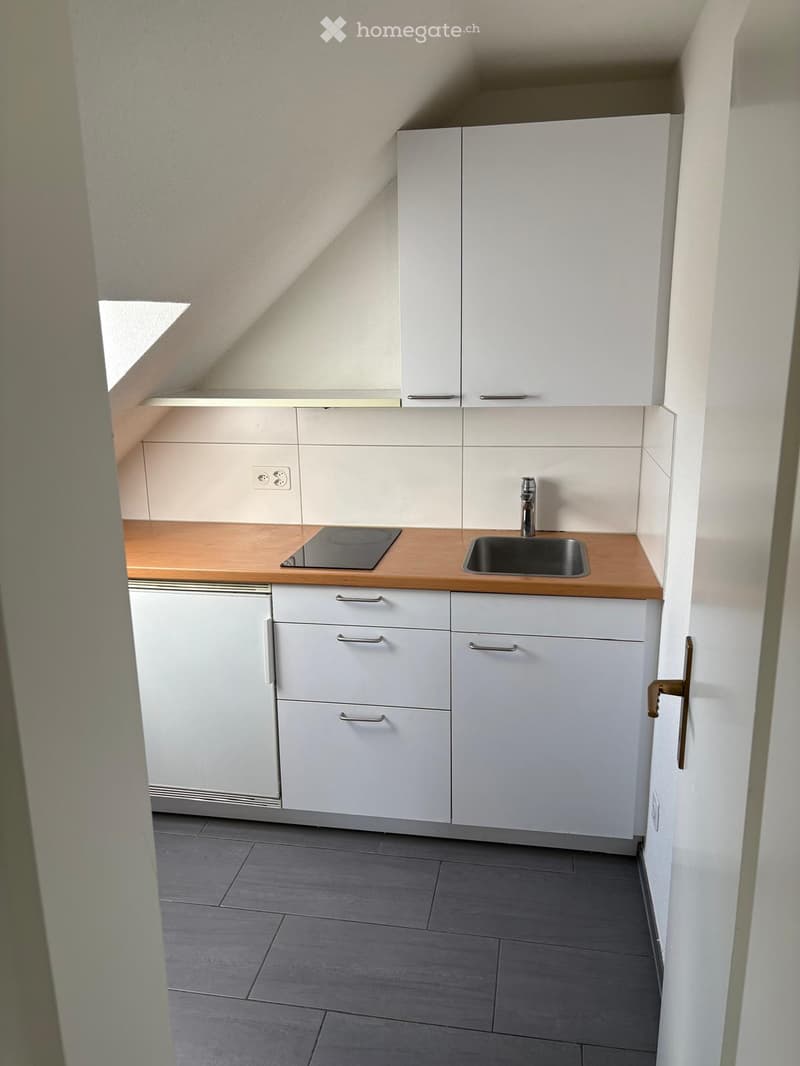 Modern kitchen with white cabinets, wooden countertop, sink, and stove. Grey tiled floor and white walls.