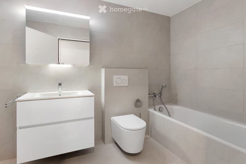 Modern bathroom with a white sink, mirror, toilet, and bathtub, featuring sleek fixtures and neutral tones.