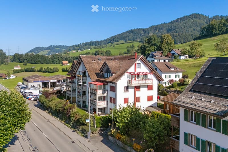 Aerial view of a residential area with multiple houses, green hills, and a clear blue sky.