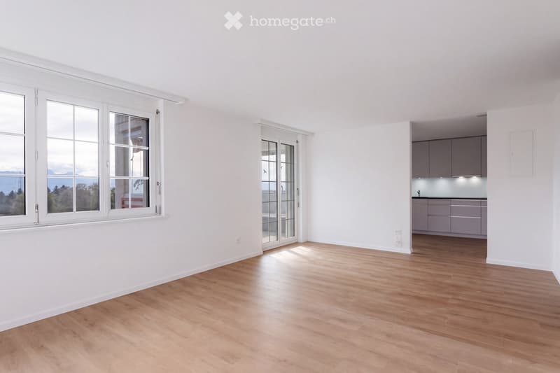 Empty room with light wooden flooring, white walls, large windows, and a view of the outdoors. The room is unfurnished and has a modern, minimalist design.