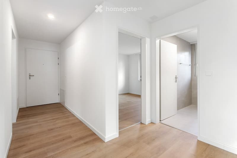 Empty hallway with white walls, wooden flooring, and two doors leading to other rooms.
