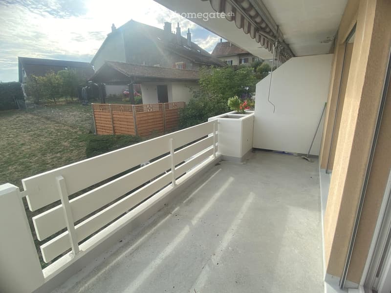 Balcony with white railing, concrete floor, and a small white planter. The view shows a fenced yard with trees and neighboring houses.