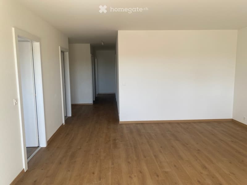Empty hallway with wooden flooring and white walls, featuring several open doors leading to other rooms.