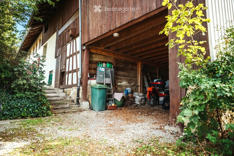 A wooden garage attached to a house, with a motorcycle parked inside, along with various tools and storage items.