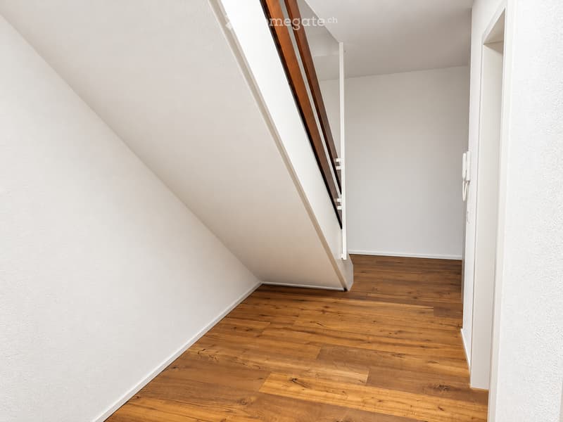 Empty room with wooden flooring and white walls, featuring a staircase leading upwards.