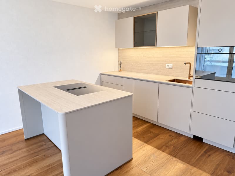 Modern kitchen with light-colored cabinets, a central island with a built-in sink, and a sleek faucet. The space features wooden flooring and built-in lighting above the counter.