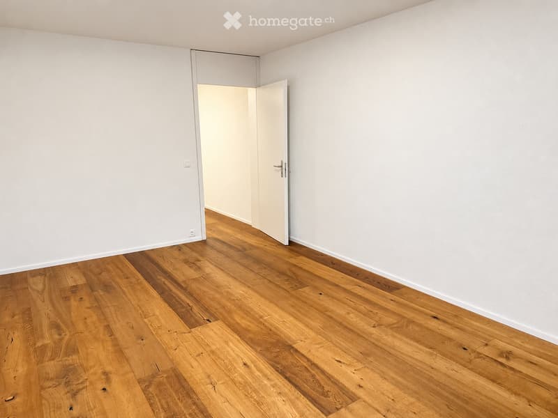 Empty room with light wooden flooring and white walls, featuring an open doorway leading to another space.