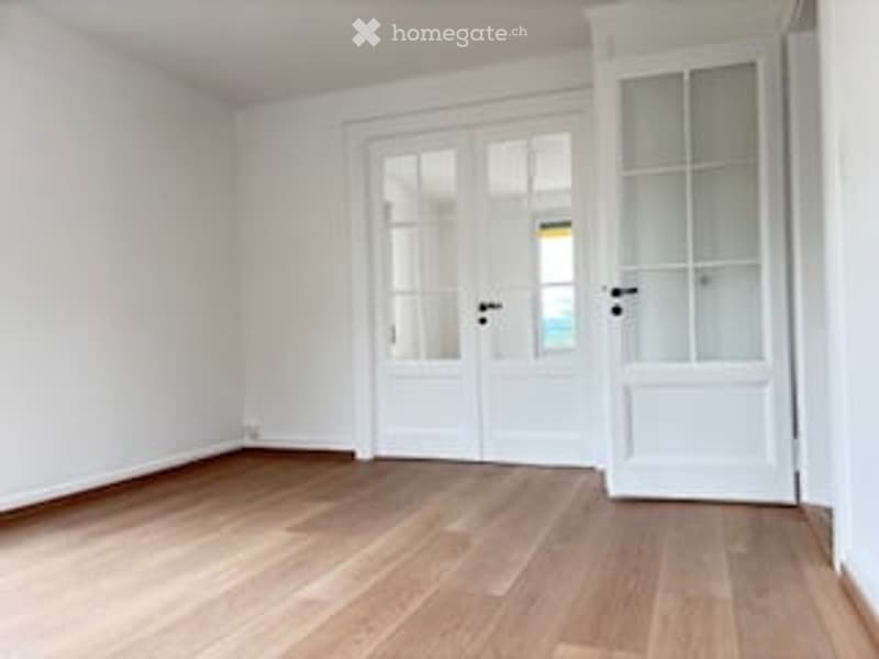 Empty room with light wooden flooring, white walls, and a white door with glass panels.