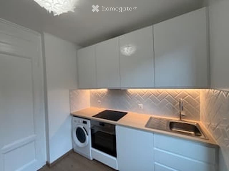 Modern, compact kitchen with white cabinets, a sink, a faucet, an oven, and a washing machine.