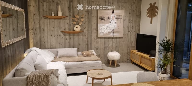 Modern living room with wooden walls, a grey sectional sofa, a small coffee table, a TV stand, a decorative stool, and a large painting on the wall.