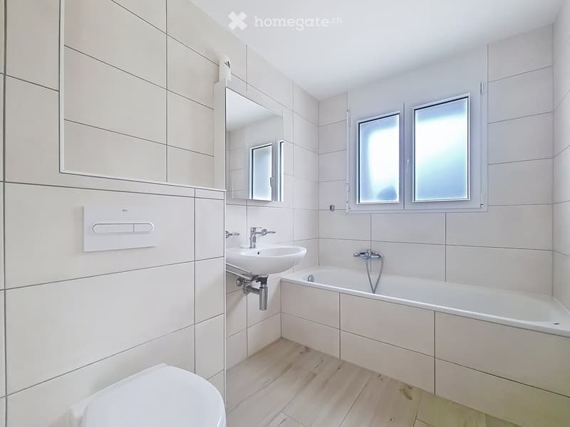 Modern bathroom with white tiles, a toilet, a sink, a bathtub, a mirror, and a cabinet.
