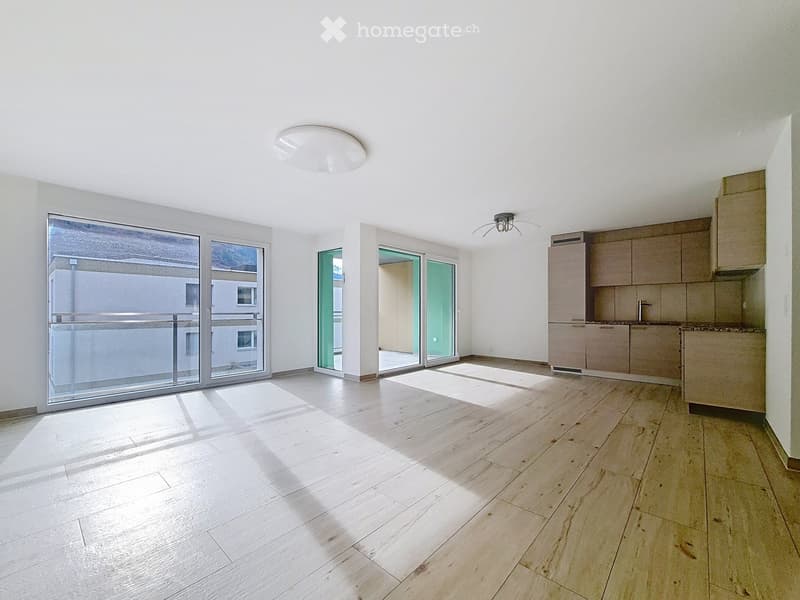 Bright, unfurnished room with wooden flooring, large windows, and sliding glass doors leading to a balcony.