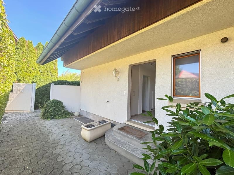 Garden area with a paved walkway, steps leading to a house entrance, potted plants, and surrounding greenery.