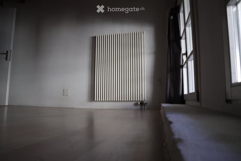 Empty room with wooden floor, white walls, radiator, and a window letting in natural light.