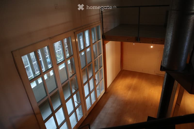 Empty room with wooden flooring, large windows, and a visible staircase leading to an upper level.
