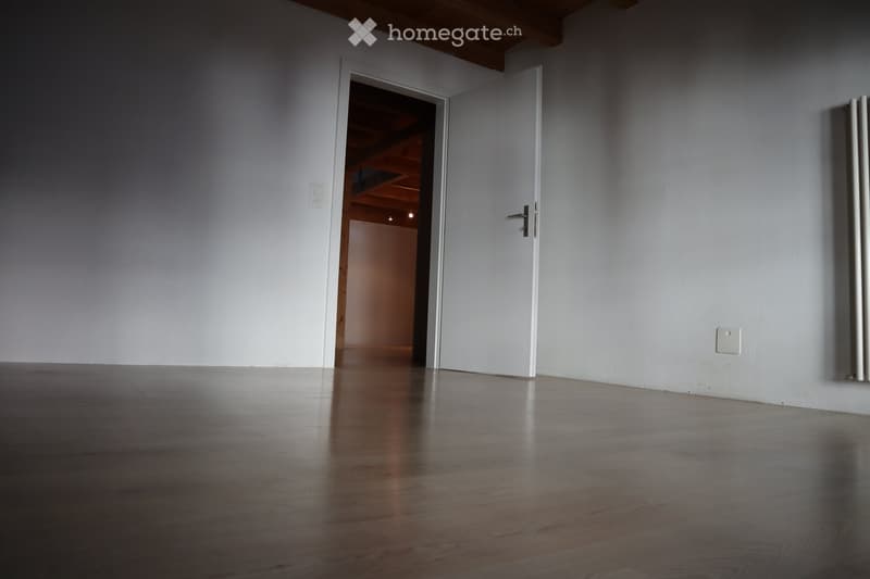 Empty room with wooden flooring, white walls, and a partially open door leading to another room.