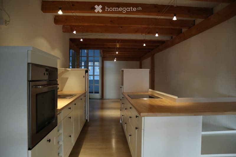Modern kitchen with white cabinets, wooden countertops, stainless steel appliances, and exposed wooden beams on the ceiling.