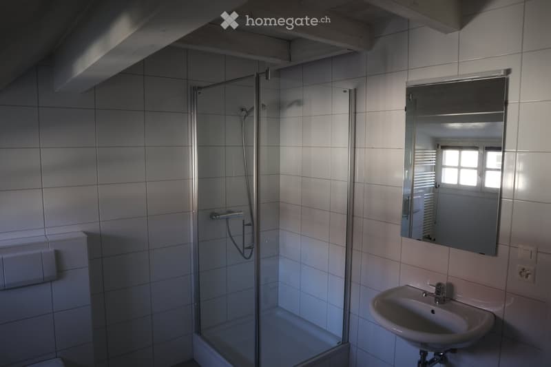 Modern bathroom with white tiled walls, a glass-enclosed shower, a sink with a mirror, and a window providing natural light.