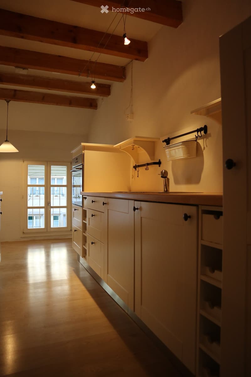 Bright kitchen with wooden cabinets, a sink, and an oven, illuminated by warm lighting and natural light from a large window.