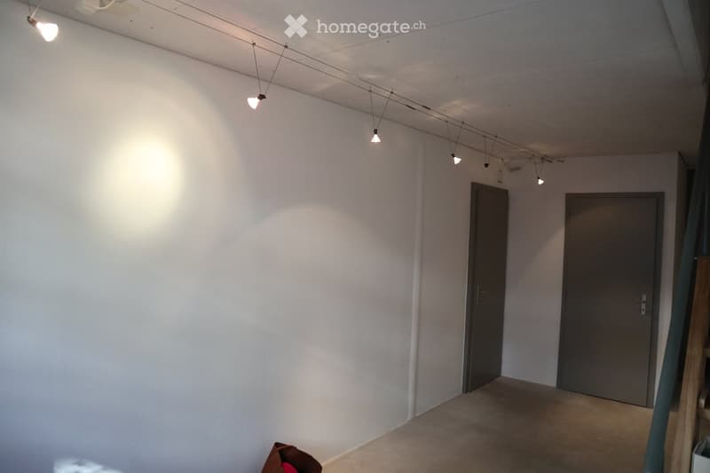 Empty room with white walls, grey doors, and track lighting. No furniture or equipment present.