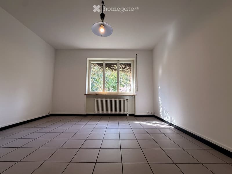 Empty room with tiled floor, white walls, a window with a radiator below, and a hanging light fixture.