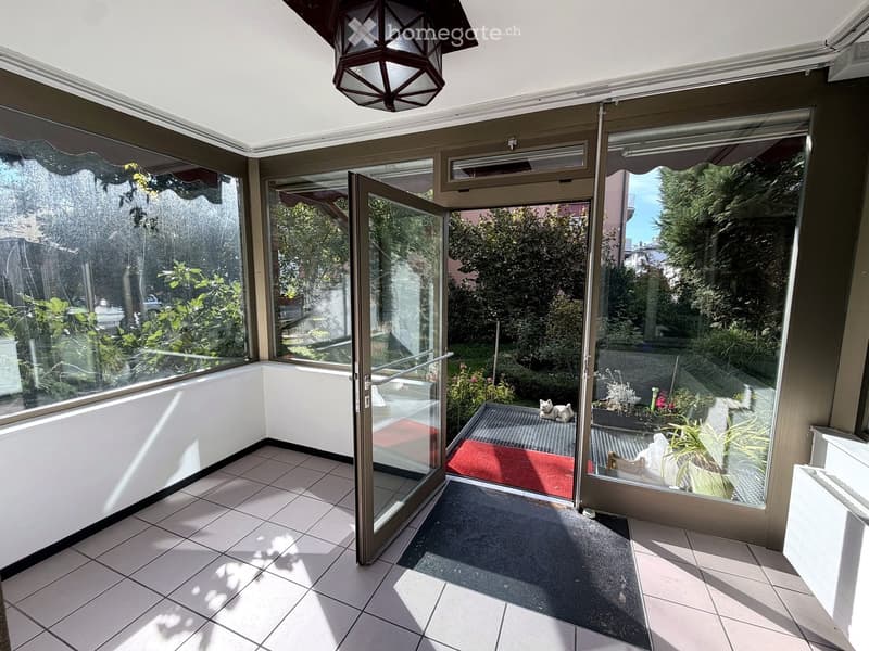 Bright, enclosed balcony with large glass windows and doors, tiled floor, and a hanging lantern light fixture.
