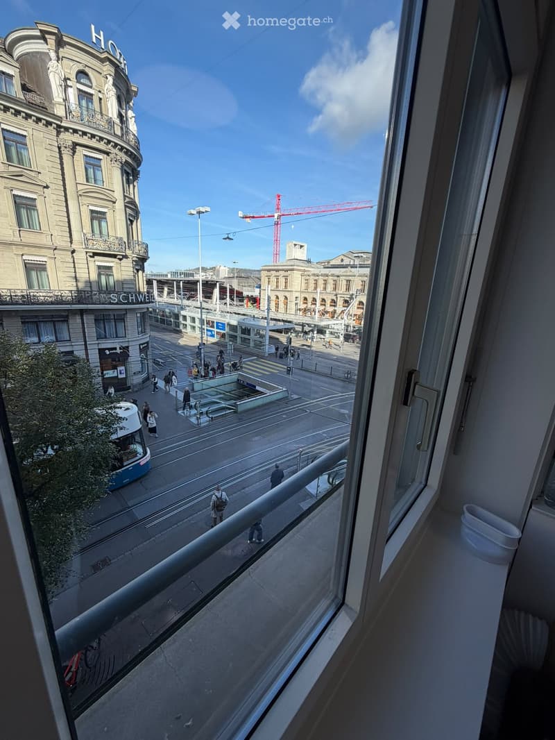 Balcony overlooking a busy urban street with pedestrians, a tram, and historic buildings.