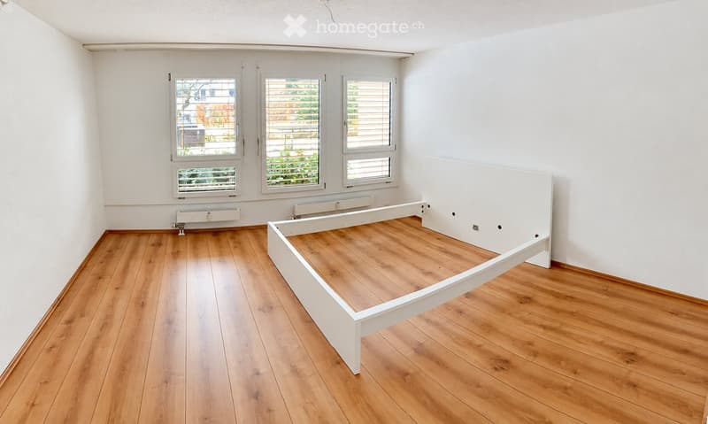 Empty room with wooden flooring, white walls, and three windows with blinds. A white bed frame is positioned against the wall.