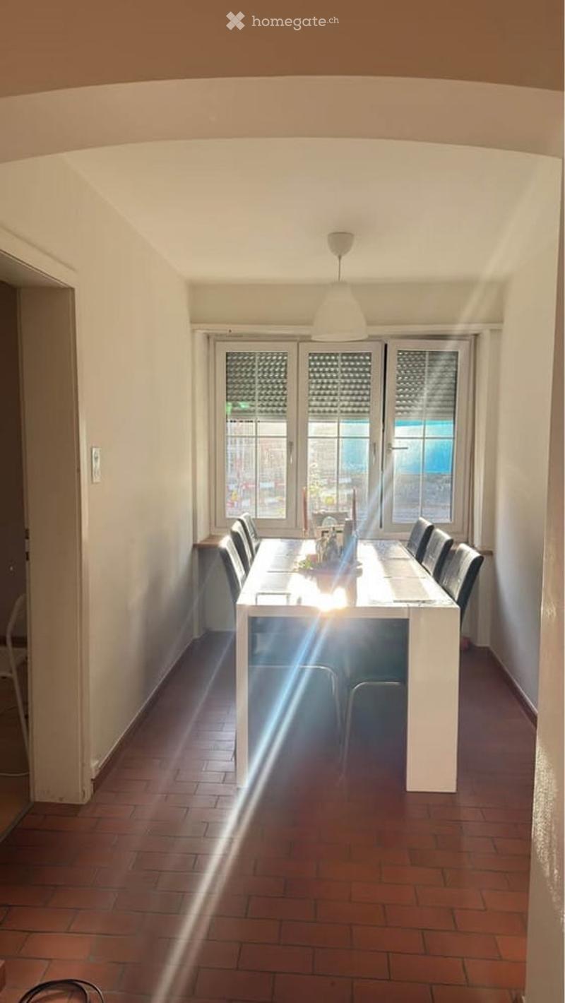 Bright dining room with a long white dining table surrounded by black chairs, a pendant light fixture, and large windows with blinds allowing natural light to flood the space.