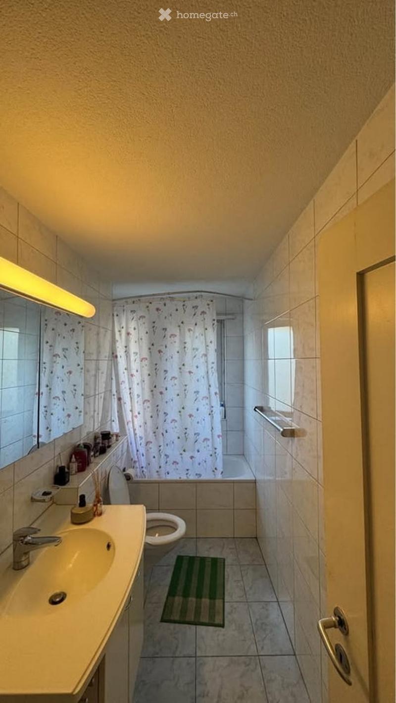 Bathroom with a sink, toilet, mirror, shower curtain, bathtub, and a small green rug on the floor.