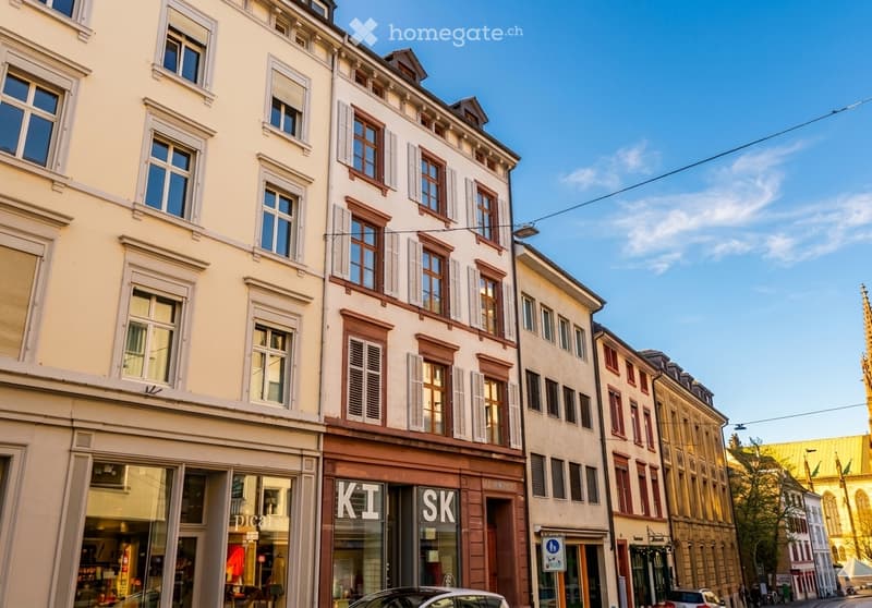A row of multi-story buildings with classic European architecture, featuring large windows, shutters, and storefronts on the ground floor.