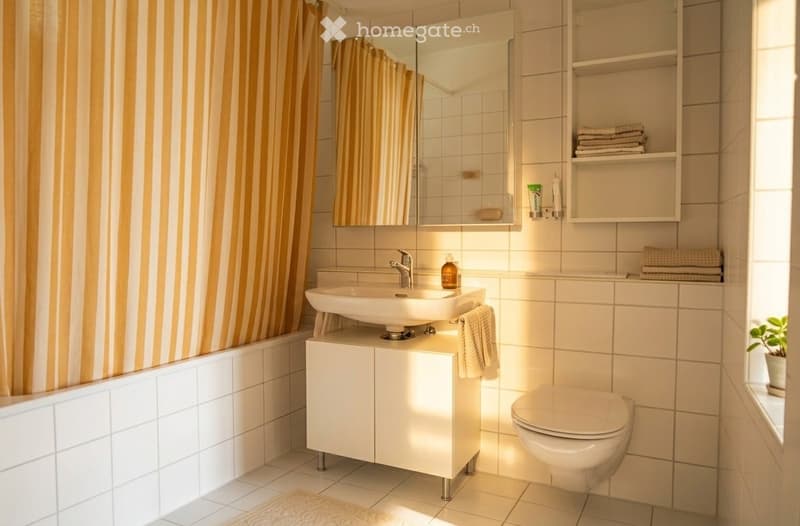 Modern bathroom with white tiles, a floating sink cabinet, a large mirror, a toilet, and neatly arranged towels and toiletries.
