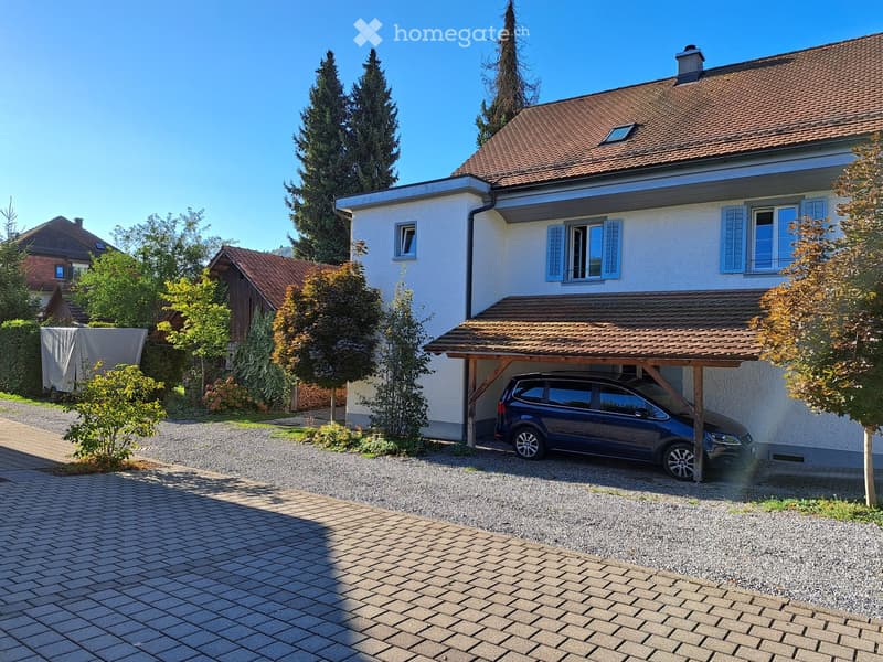 Two-story house with white exterior, blue shutters, and a covered garage with a parked car.