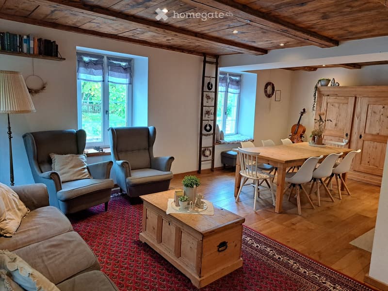 Cozy living and dining area with wooden beams, hardwood floors, large windows, sofa, armchairs, coffee table, dining table, and chairs.