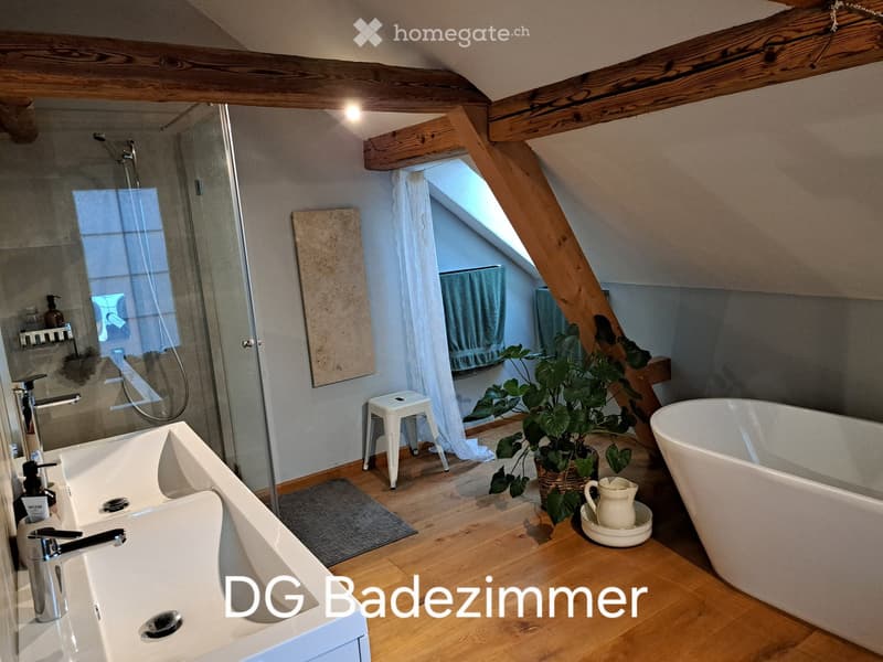 Modern bathroom with wooden beams, a large sink, a bathtub, a shower area, a small white stool, a potted plant, and a decorative pitcher on the floor.