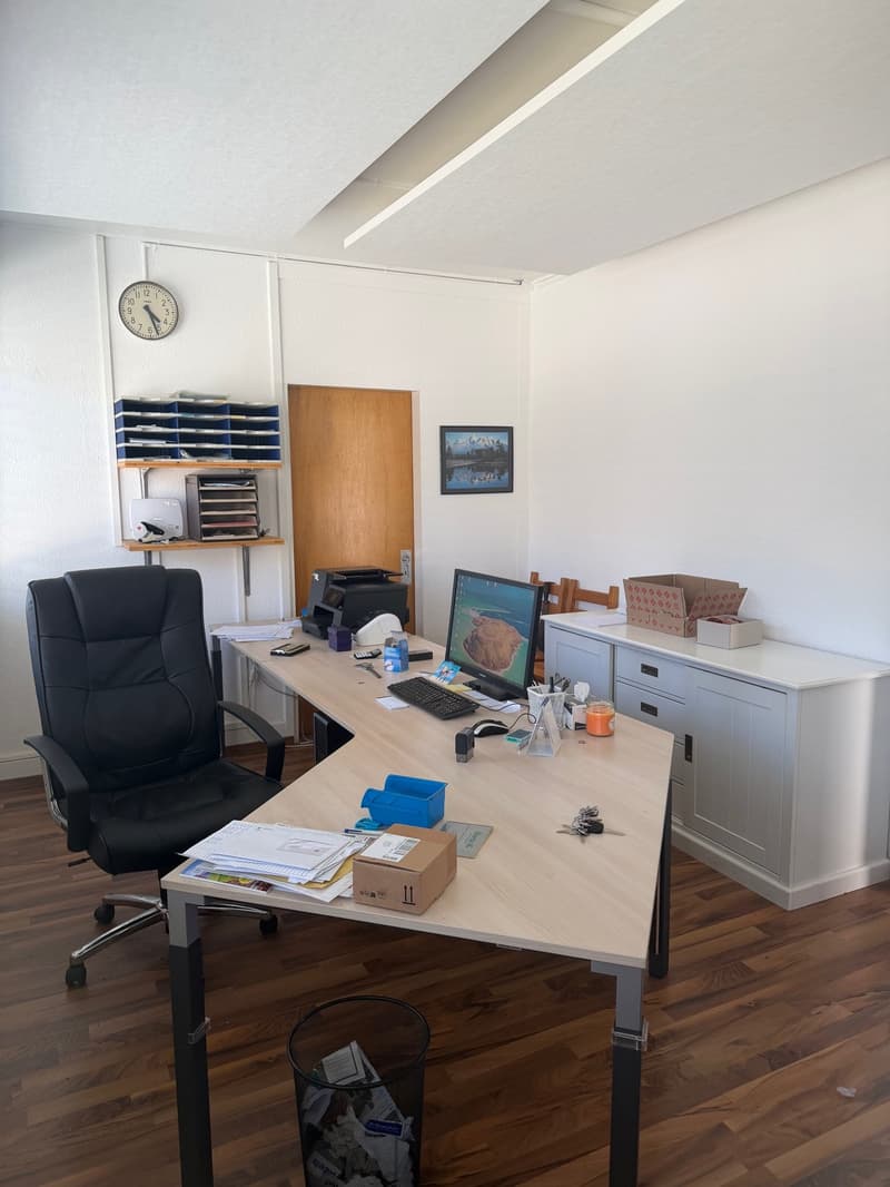 An office with a desk, office chair, computer monitor, keyboard, mouse, printer, boxes, trash can, clock, picture frame, cabinet, remote control, cell phone, calculator, bottle, candle, tissue box, keys, binder, envelopes, and binder clips.