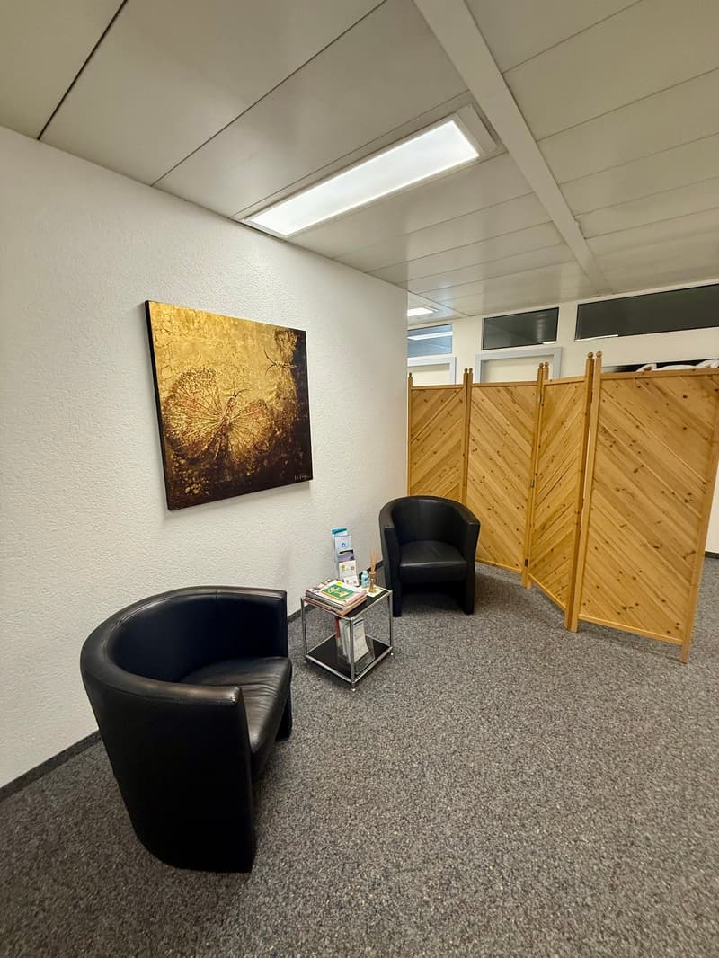 modern waiting room with black leather chairs, desk with books, wooden divider, art painting on wall