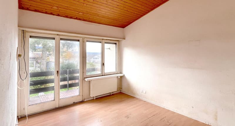 Empty room with sliding doors, wooden floor, windows, balcony, radiator, power outlets