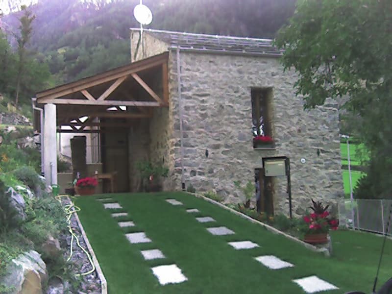 Stone house, wooden porch, green lawn, flower pots, mountain view