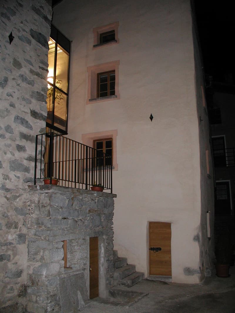Stone wall, white wall, wooden door, stairs, balcony with railings, potted plants