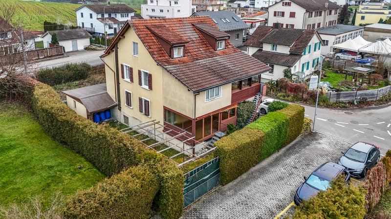 2-story house, red roof, multiple windows, surrounded by greenery, small garden, 2 cars parked