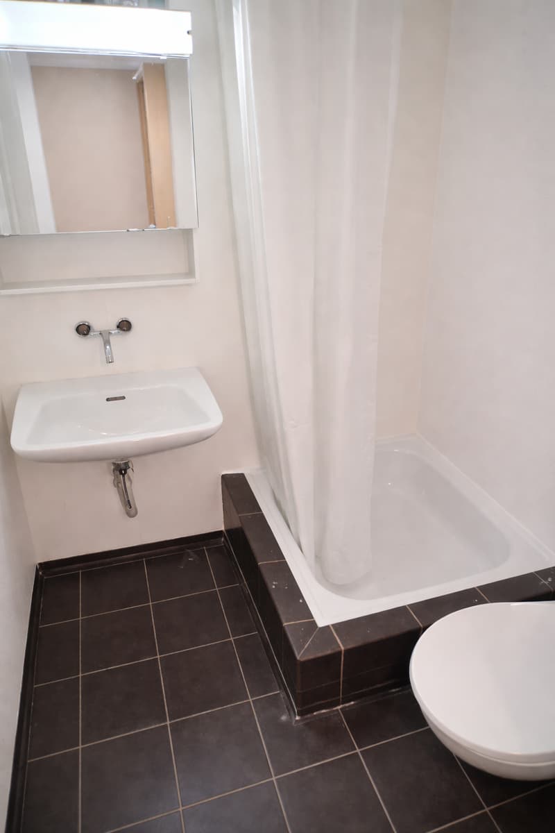 white sink, white bathtub, white shower curtain, white toilet, mirror, black tiles