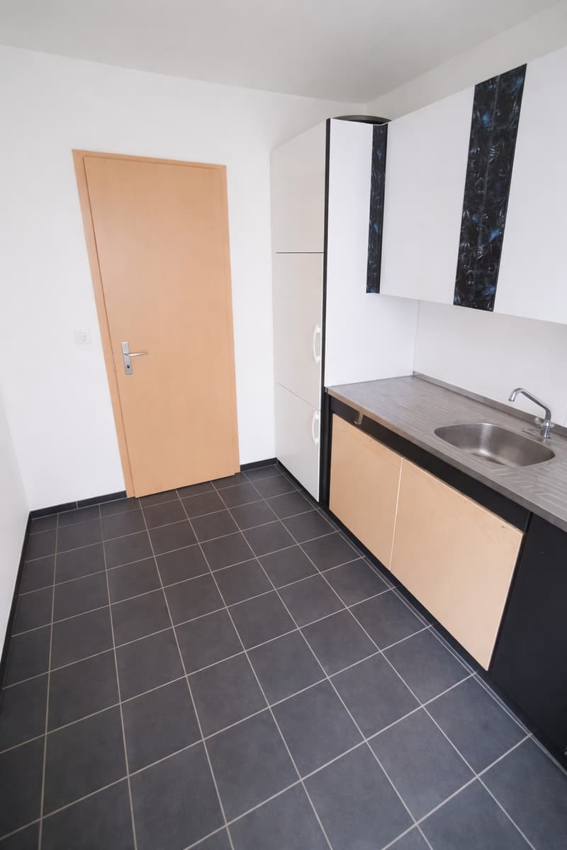 empty kitchen with tiled floor, white cabinets, stainless steel countertop, sink, faucet, wooden door