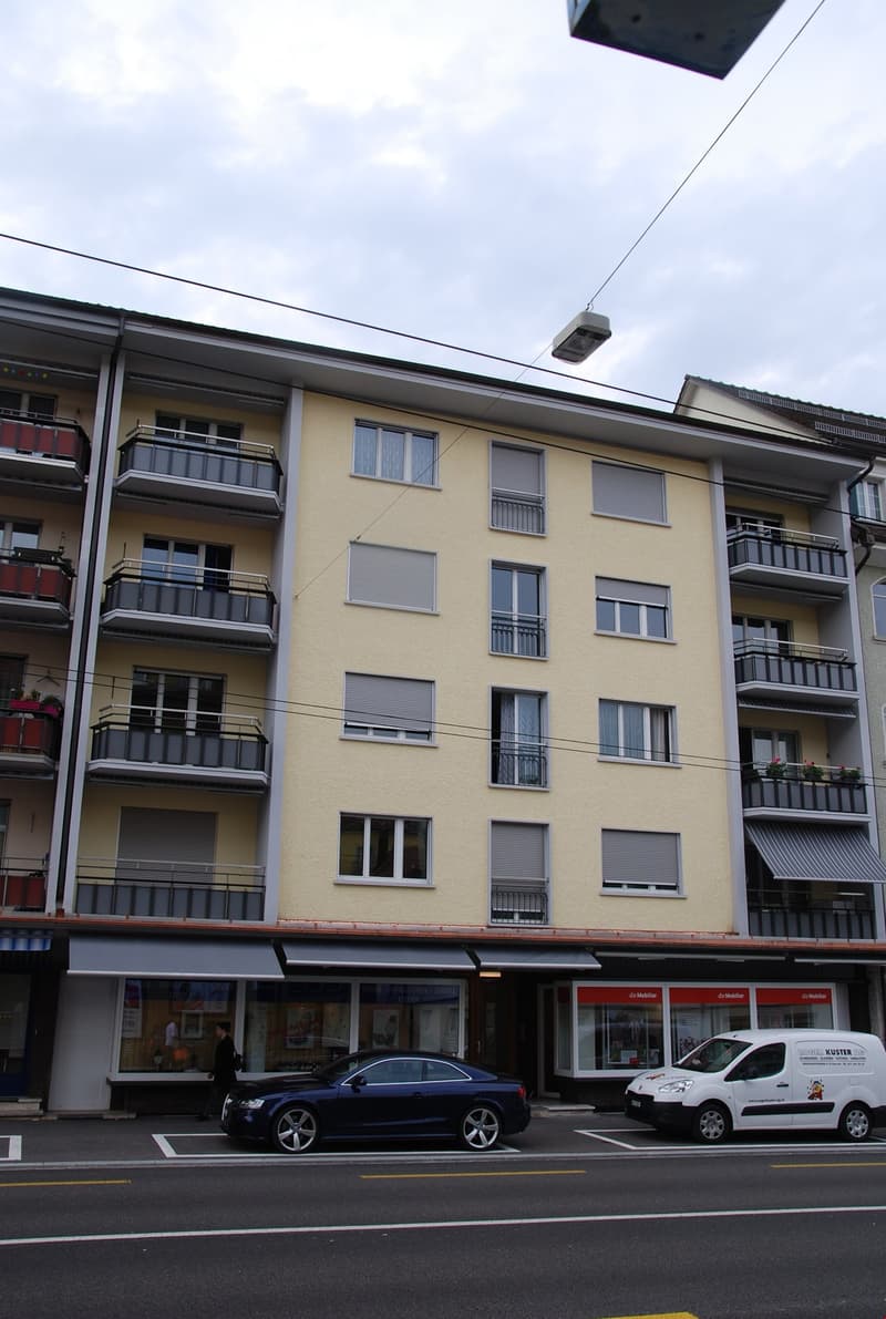 5 story building, yellow exterior, multiple balconies, storefronts on the ground floor