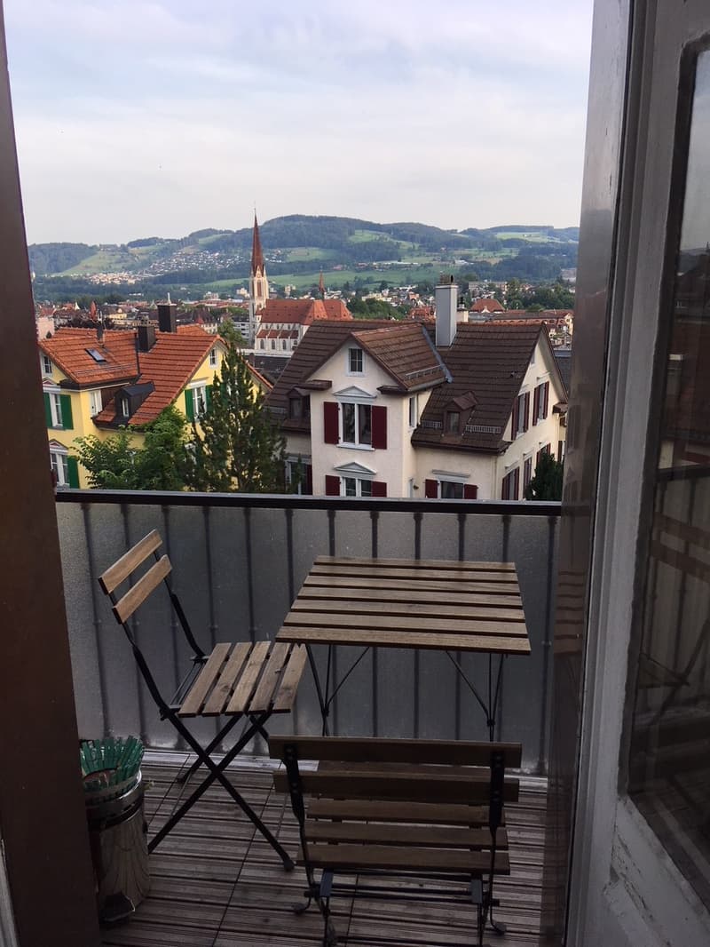 Balcony with table and chairs, metal railing, wooden floor, view of the town