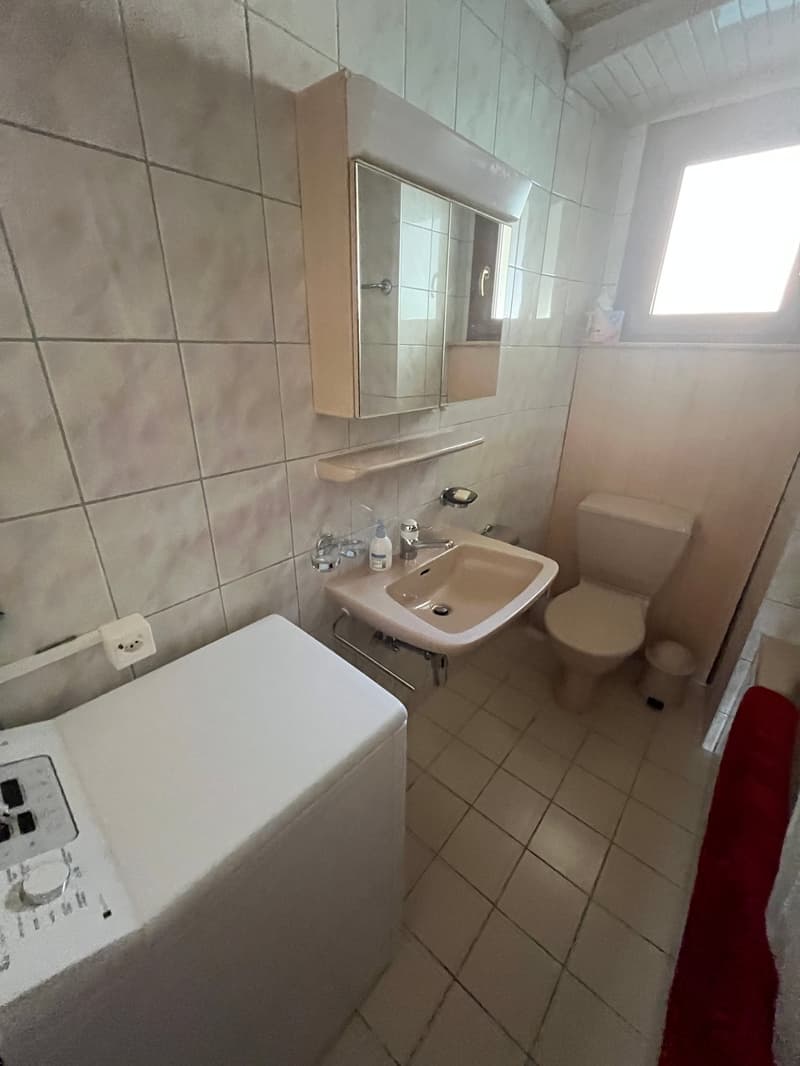 Bathroom with white tiles, sink, toilet, washing machine, mirror, and window
