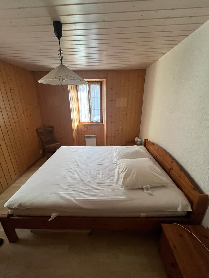 Bedroom with wooden walls, bed, chair, window, lamp, and wooden nightstand