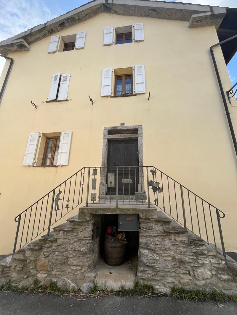 2 story house, yellow exterior, white shutters, stone steps, wooden door, barrel
